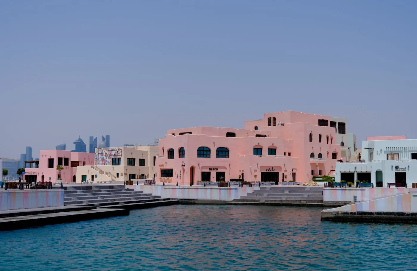 Pastel-coloured waterfront buildings in Doha with the city skyline in the distance